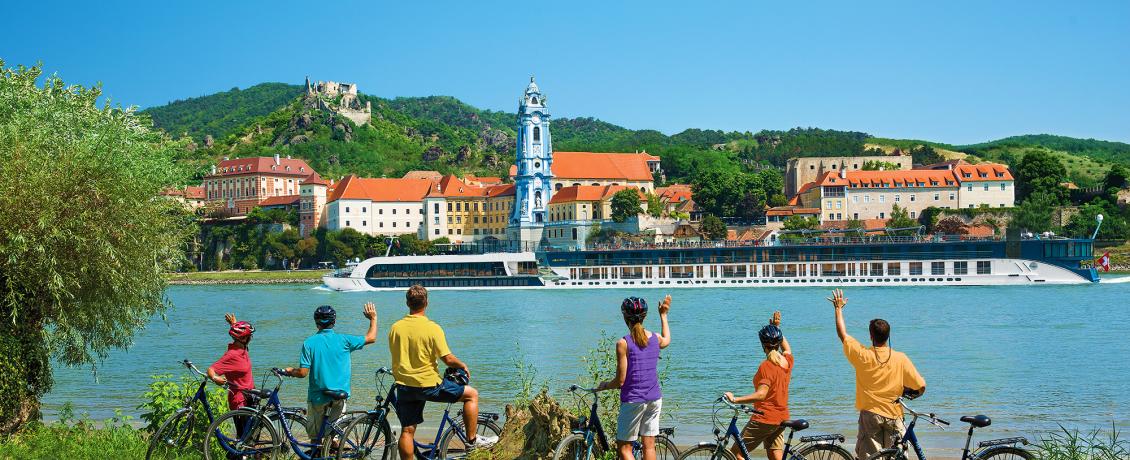 Travellers on a bike tour waving across to the ship with Durnstein Abbey in the background