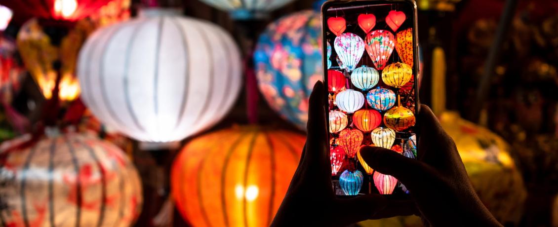 Silhouette of a person holding a phone and photographing vibrant lanterns in Hoi An