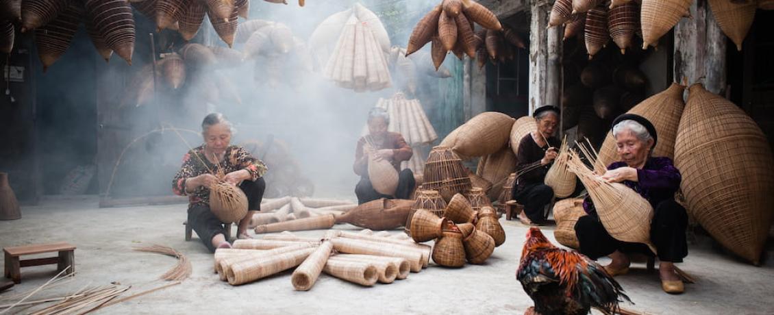 Women weaving baskets surrounded by woven baskets and a rooster