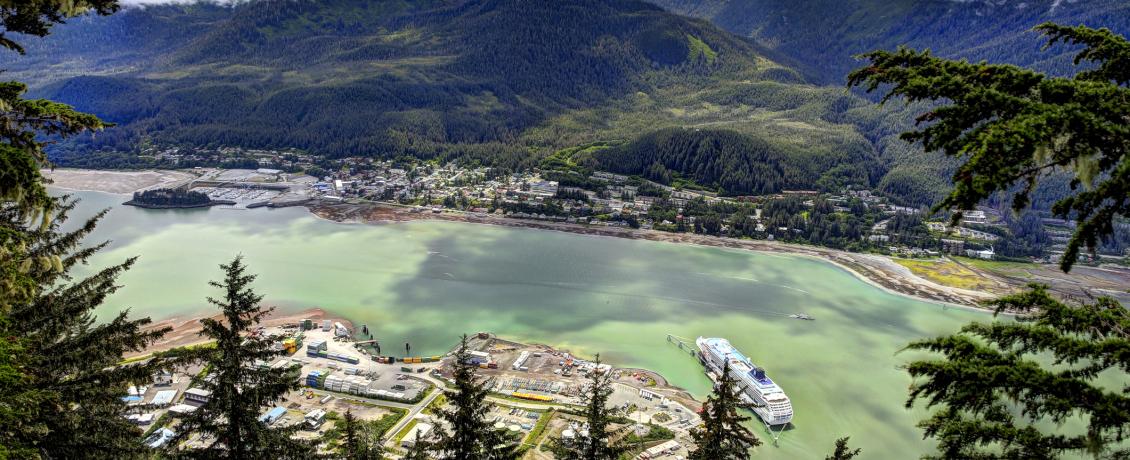 Aerial view of Juneau, Alaska surrounded by forests and a lake with a cruise ship below and mountains in background