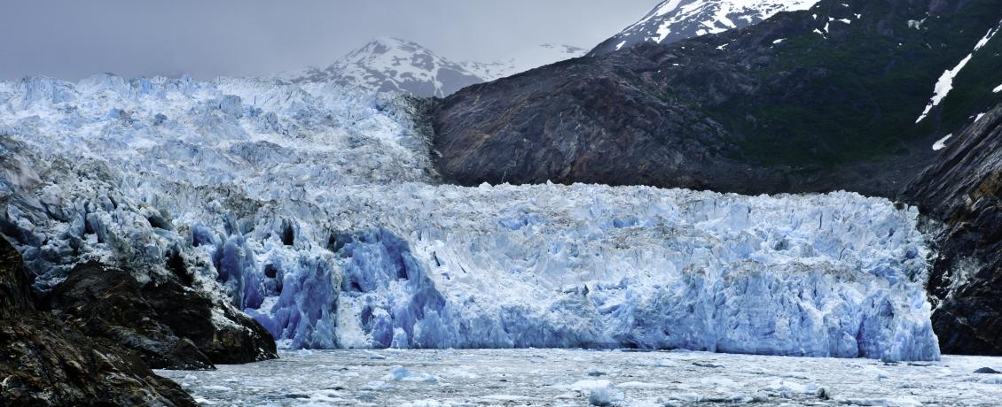 Sawyer Glacier, a bright blue frozen glacier, spans the end of Alaska's steep, forested Tracy Arm Fjord