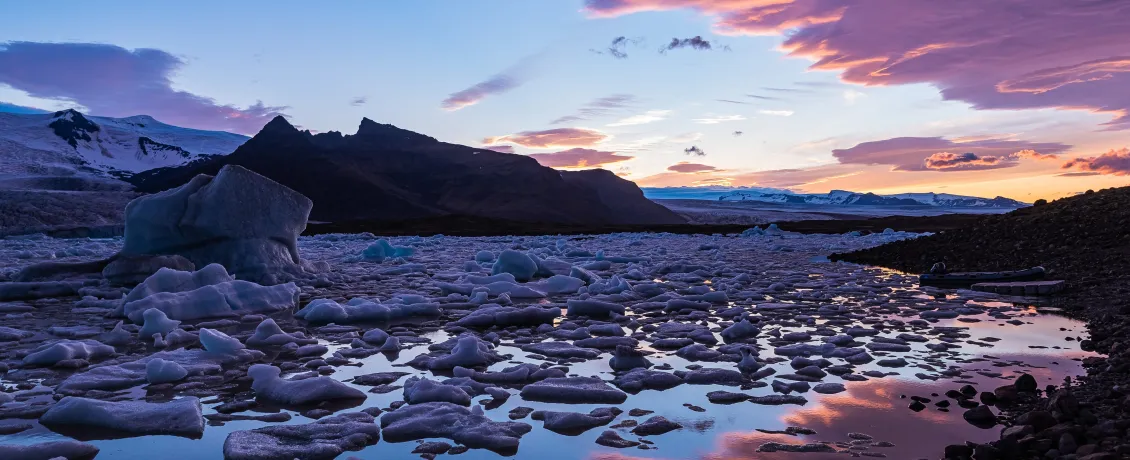 Sunset casts pink and blue hues over a glacier lagoon with floating icebergs and distant mountains in Iceland