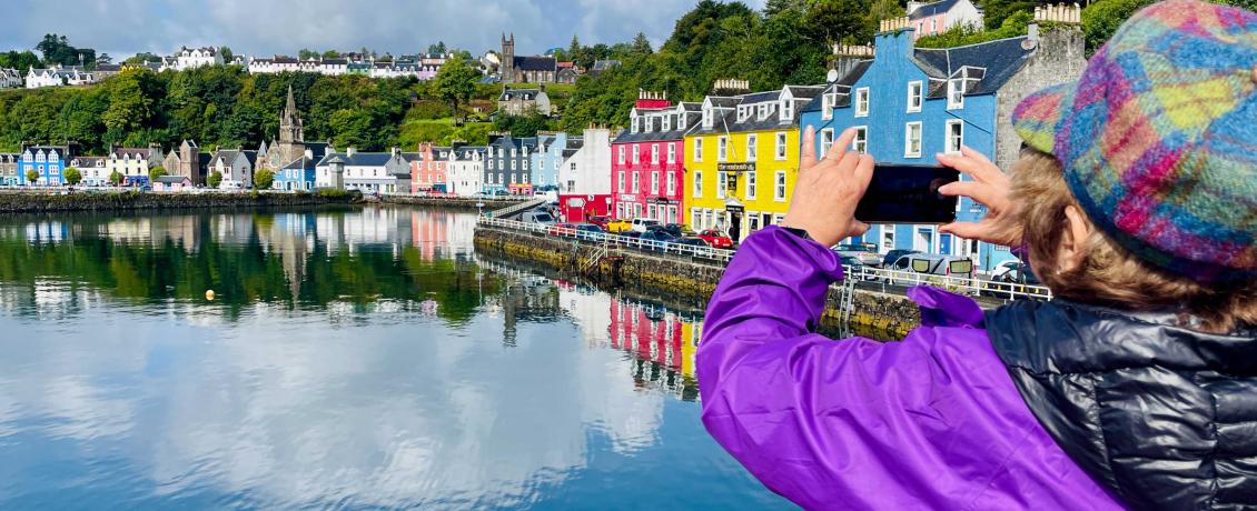 Traveller photographing colourful waterfront buildings in Tobermory on the Isle of Mull.