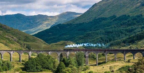 Steam train crossing the Glenfinnan Viaduct amid the mountains of the Scottish Highlands.